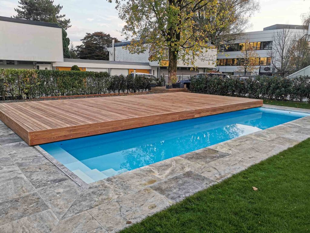 Exklusive Terrassen Design Riegler Poolabdeckung, die offen einen einladenden Pool und geschlossen eine stabile Holzterrasse zeigt.