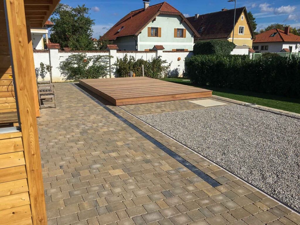 Terrassen Design Riegler präsentiert eine nahtlos integrierte Poolabdeckung, die als Holzterrasse dient und den Gartenbereich aufwertet.